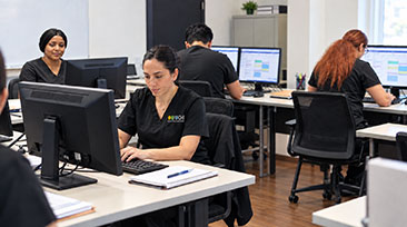 Students in SOCHI uniforms working at desktop computers in a classroom for CMAA training.