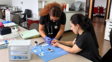 SOCHI medical assistant students practicing a finger-stick technique with medical supplies in a classroom.